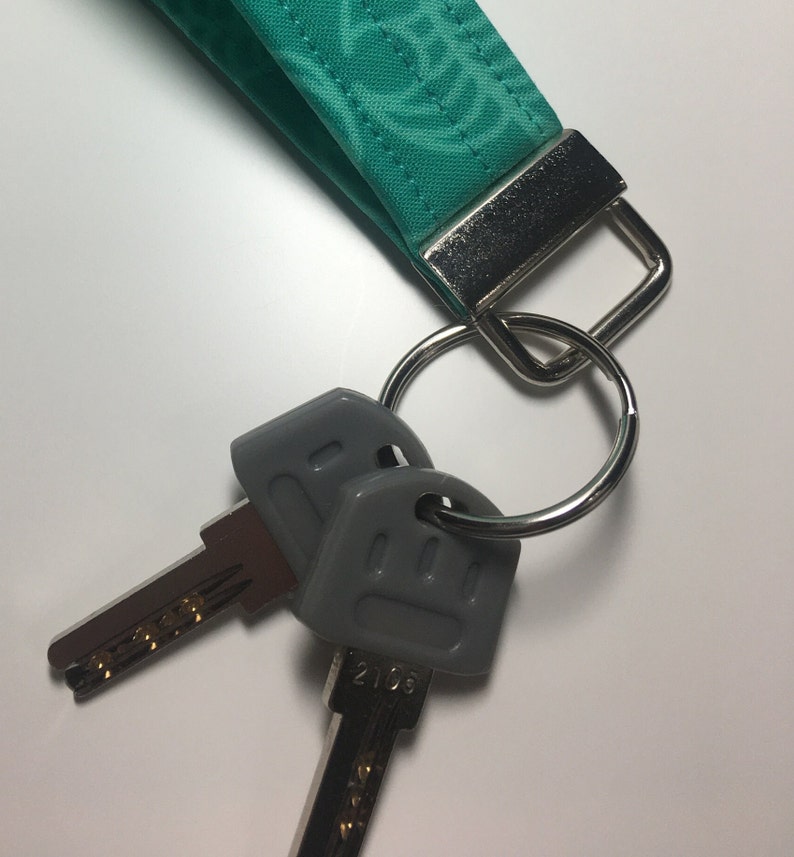 May include: A teal fabric keychain with a silver ring and two gray keys. One key has the number 2106 printed on it.