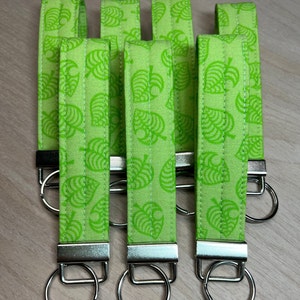 May include: Six green fabric keychains with a white leaf pattern and silver key rings.
