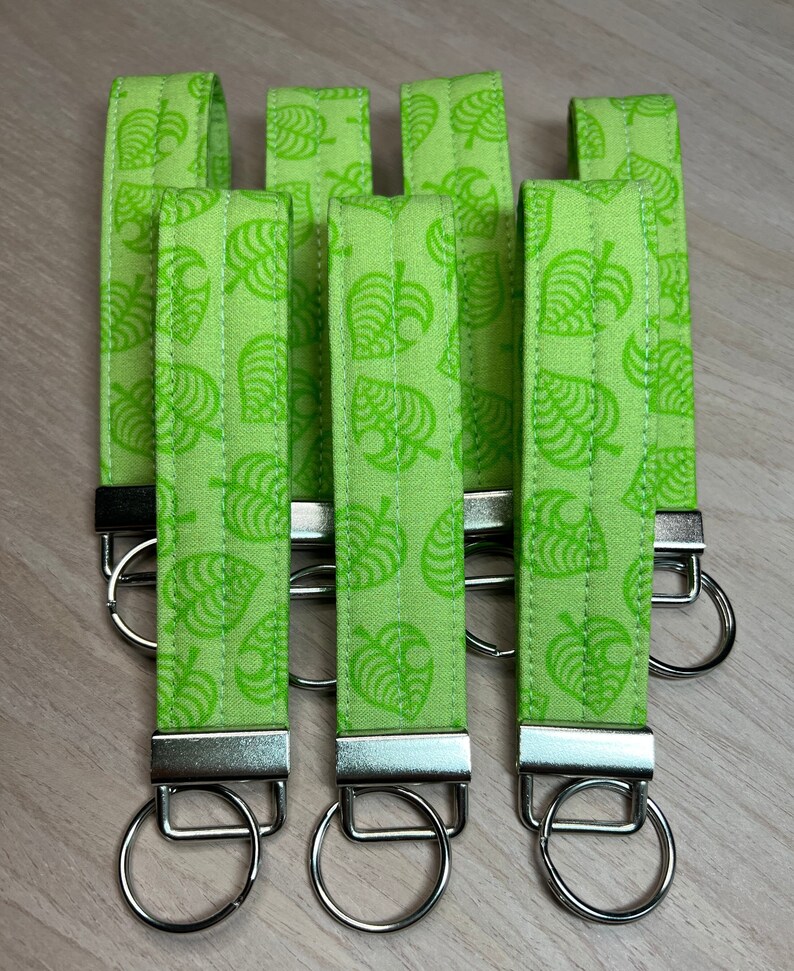 May include: Six green fabric keychains with a white leaf pattern and silver key rings.