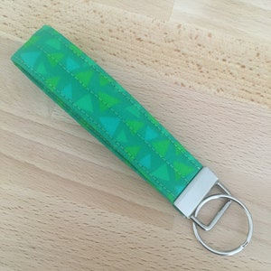 May include: A green and white patterned fabric keychain with a silver key ring. The fabric has a geometric pattern of triangles.