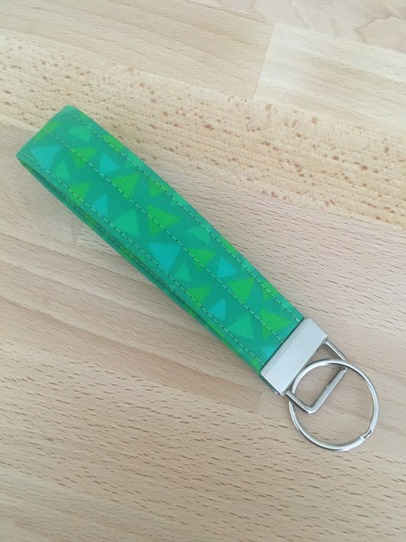 May include: A green and white patterned fabric keychain with a silver key ring. The fabric has a geometric pattern of triangles.