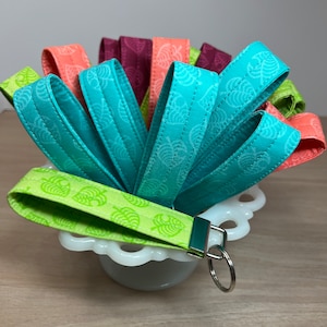 May include: A set of colorful fabric keychains with a leaf pattern. The keychains are in shades of green, blue, and pink. The keychains are arranged in a bowl.