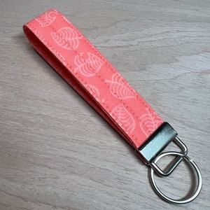 May include: A pink fabric keychain with a white leaf pattern and a silver key ring.