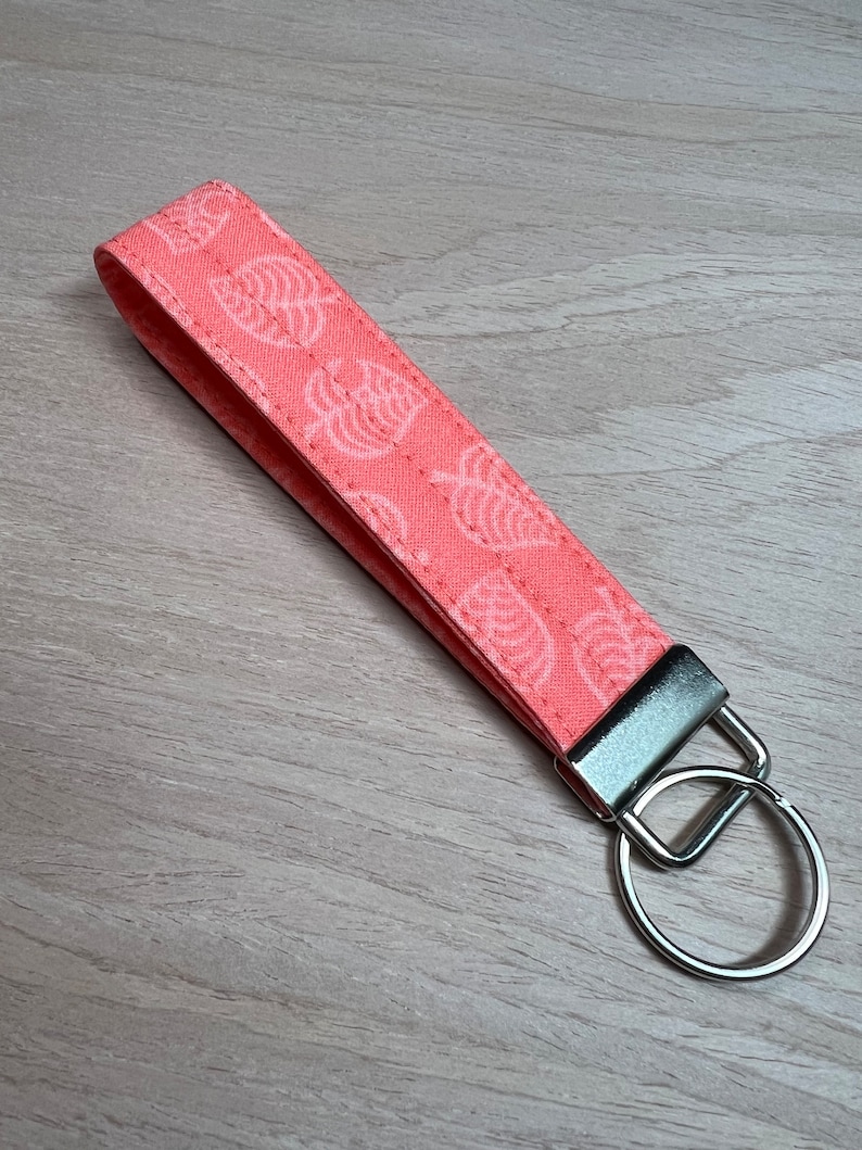 May include: A pink fabric keychain with a white leaf pattern and a silver key ring.