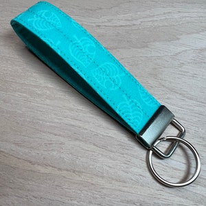 May include: A turquoise blue fabric keychain with a white leaf pattern and a silver metal ring.