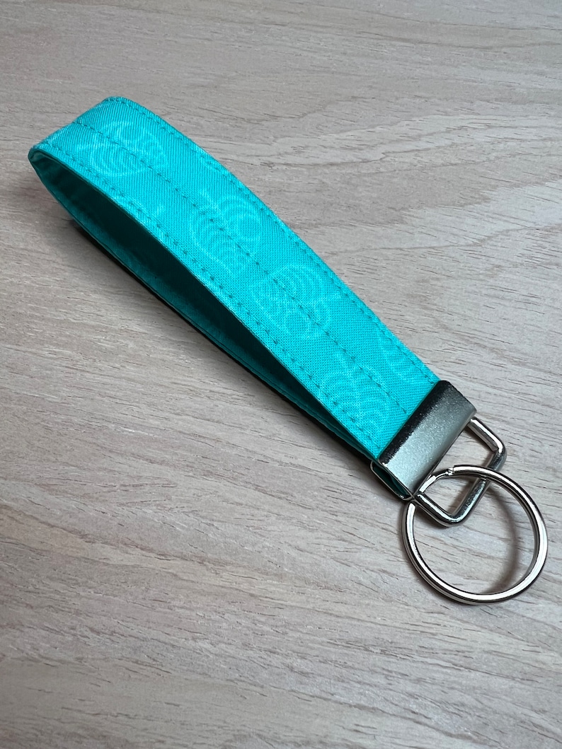 May include: A turquoise blue fabric keychain with a white leaf pattern and a silver metal ring.