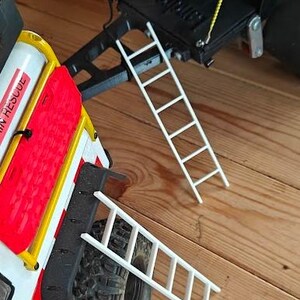 May include: A model rescue vehicle featuring a yellow inflatable raft and a small white ladder. The vehicle has red and white detailing and a black tyre. The raft has the word "RESCUE" on it.
