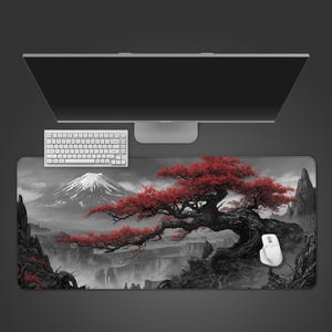 May include: A large rectangular mouse pad featuring a black and white landscape with a red-leafed tree and a snow-capped mountain. A white keyboard and mouse are visible. The pad is designed to sit under a computer monitor.