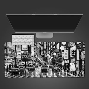 May include: Black and white desk mat featuring a pixelated illustration of a rainy Japanese street scene with cars, pedestrians, and neon signs. A white keyboard and mouse are visible.