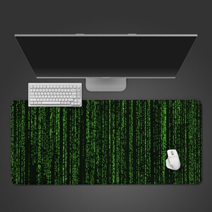May include: A computer setup featuring a large monitor, white keyboard, and mouse. The focus is on a rectangular mousepad with a black background and a green, vertical, digital rain pattern, creating a tech-inspired aesthetic.
