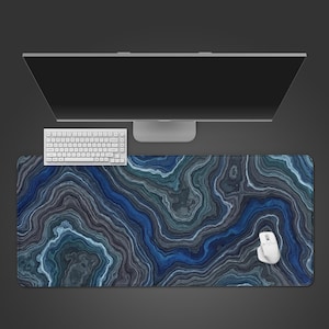 May include: A large, rectangular mouse pad with a blue, gray, and white agate stone pattern. A white keyboard, mouse, and computer monitor are on top of the pad. The pad is designed for use with a computer.