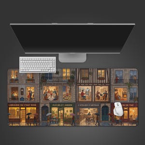 May include: A rectangular mouse mat with a detailed illustration of a European street scene with shops and apartments. The scene includes people, umbrellas, and shop signs. A white keyboard and mouse are visible.