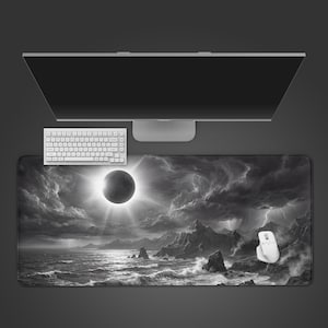 Puede incluir: Alfombrilla de ratón en blanco y negro con un dramático paisaje marino y un eclipse solar. Un teclado y un ratón blancos están colocados sobre la alfombrilla, con un monitor de ordenador en el fondo. El diseño incluye montañas, nubes tormentosas y olas.