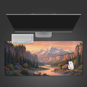 May include: A rectangular desk mat featuring a printed landscape illustration of a winding river flowing through a valley with snow-capped mountains, rocky cliffs, and dense pine forests under a soft orange and pink sunset sky.