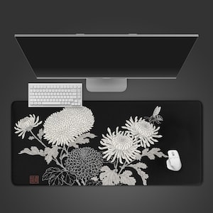Może przedstawiać: Czarna prostokątna podkładka pod mysz z kwiatowym wzorem z białymi chryzantemami i pszczołą. Widoczna jest biała klawiatura i mysz. Podkładka ma dekoracyjny, artystyczny styl.