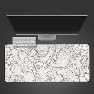 Peut inclure: Un tapis de bureau rectangulaire à surface blanche orné d'un motif de lignes de carte topographique noires. Le tapis est placé sous un clavier d'ordinateur blanc et une souris blanche, avec un écran d'ordinateur situé au-dessus du clavier.