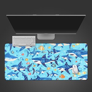 May include: A blue mouse mat with a pattern of sharks and fish. The sharks are decorated with blue and white patterns. The background is light blue with additional fish and aquatic plants. A white keyboard and mouse are visible.