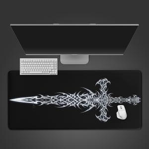 May include: Black rectangular desk mat featuring a white tribal sword design. A white keyboard and mouse are positioned near the mat. A computer monitor is in the background.