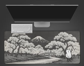 May include: A rectangular desk mat featuring a black and white illustration of a landscape with Mount Fuji, cherry blossom trees, a river, and a small arched bridge. A white computer keyboard and a white computer mouse sit on the mat.