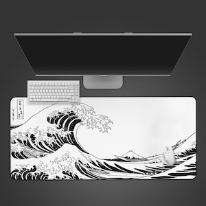 May include: A rectangular desk mat featuring a black and white graphic print of a large ocean wave and a mountain in the background. The design includes traditional Japanese-style calligraphy in the upper left corner. A white computer mouse sits on the mat.