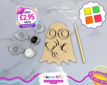 Puede incluir: Un kit de manualidades con una forma de fantasma de madera, botes de pintura, un pincel y una paleta de colores. El kit incluye el texto "Your Colour, Your Creation!". La marca es Cosmic Kits.