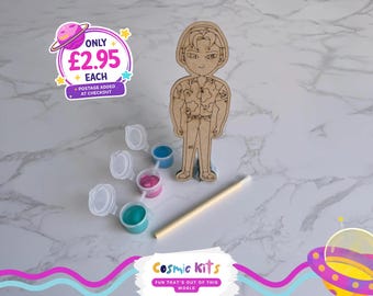 May include: A wooden figure of a person with a floral shirt, paint pots with blue, pink, and teal paint, and a paintbrush. The image also includes the text "Cosmic Kits" and "FUN THAT'S OUT OF THIS WORLD".