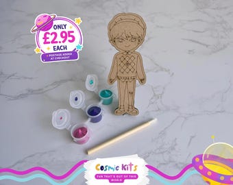 May include: A wooden figure of a person with a paint-your-own kit. The kit includes small paint pots with various colors and a wooden paintbrush. The image also features the text "Cosmic Kits FUN THAT'S OUT OF THIS WORLD."