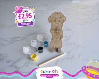 Puede incluir: Una figura de madera, botes de pintura amarilla, negra y azul, y un pincel. La imagen incluye el texto "Cosmic Kits FUN THAT'S OUT OF THIS WORLD".