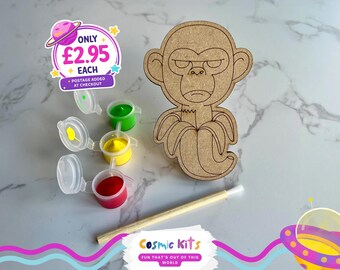 Puede incluir: Un kit de manualidades de madera con forma de mono con un plátano, botes de pintura roja, amarilla y verde, y un pincel. El kit incluye el texto "Cosmic Kits" y "Fun that's out of this world."