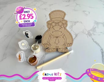 Puede incluir: Un kit de manualidades con una figura de madera de un hombre con sombrero de copa y gafas, con botes de pintura y un pincel. La imagen incluye el texto "Cosmic Kits" y "FUN THAT'S OUT OF THIS WORLD".