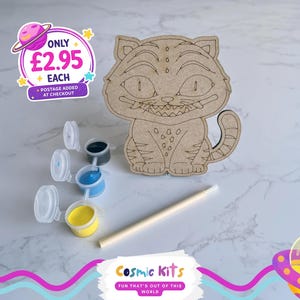 May include: A wooden Cheshire Cat craft kit with paint pots in blue, yellow, and black, and a paintbrush. The kit includes a wooden cat cutout with engraved details. The Cosmic Kits logo is visible.