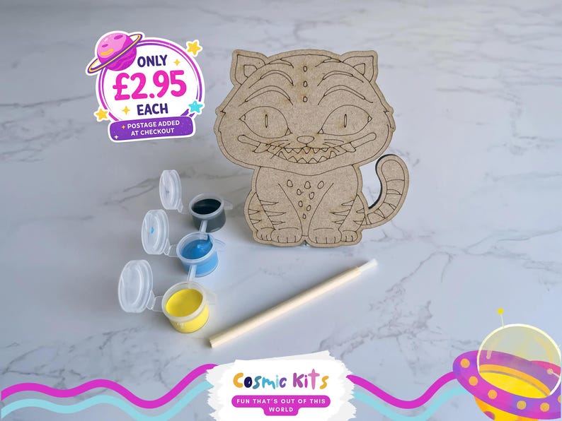 May include: A wooden Cheshire Cat craft kit with paint pots in blue, yellow, and black, and a paintbrush. The kit includes a wooden cat cutout with engraved details. The Cosmic Kits logo is visible.