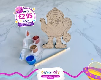 Puede incluir: Un kit de manualidades de madera con forma de tetera con una cara, acompañado de pequeños botes de pintura en rojo, marrón y azul, y un pincel. El kit es de Cosmic Kits, con el texto "FUN THAT'S OUT OF THIS WORLD".