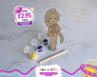Puede incluir: Una figura de madera con un peinado trenzado, un kit de pintura con pinturas amarillas, moradas y azules, y un palito de madera. La imagen también incluye el texto "Cosmic Kits" y "FUN THAT'S OUT OF THIS WORLD".