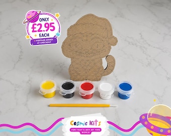 Puede incluir: Un kit de manualidades con forma de gato de madera con un gorro de Papá Noel, botes de pintura en amarillo, negro, rojo, blanco y azul, y un pincel. El kit incluye el texto "Cosmic Kits" y "Fun that's out of this world".