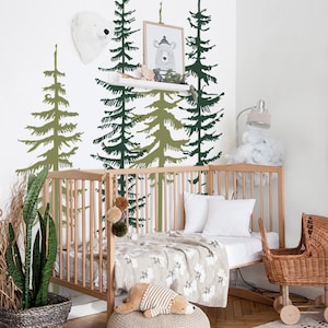 May include: A wooden crib with a white sheet and a beige blanket. The crib is decorated with a green and brown forest wall decal. There is a stuffed animal on the bed and a wicker doll stroller next to the crib.