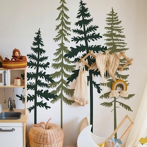 May include: A white wall with a forest scene of dark green trees, a white wicker basket with a mesh bag hanging from it, a white wooden doll stroller, and a wicker basket shaped like an apple.