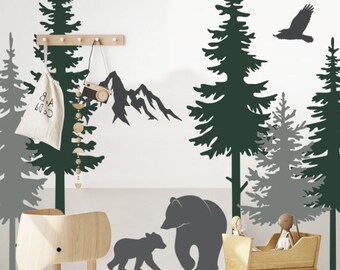 May include: A nursery room with a woodland theme featuring a black and gray bear and cub silhouette, a gray and green pine tree silhouette, and a black bird silhouette. The room also features a wooden rocking cradle, a wooden elephant toy, and a black and white road rug.