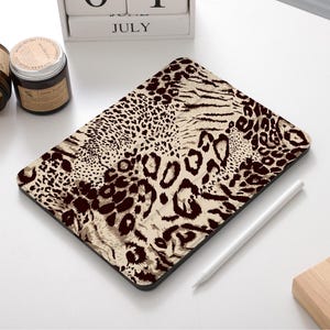 Può includere: Una custodia rettangolare per tablet con un motivo animalier marrone e beige. Il design presenta motivi di leopardo e strisce di tigre. Sono visibili anche uno stilo bianco e due barattoli di vetro marrone.