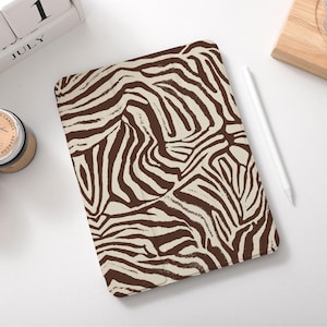 May include: A rectangular tablet case with a brown and cream zebra stripe pattern. A white stylus rests beside the case. A calendar shows July 1. Two scented candles are also in the image.