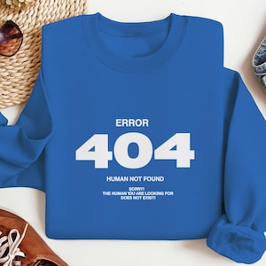 Könnte beinhalten: Ein königsblaues Sweatshirt mit dem weißen Text "ERROR 404 HUMAN NOT FOUND". Der Text "SORRY! THE HUMAN YOU ARE LOOKING FOR DOES NOT EXIST!" ist ebenfalls weiß dargestellt. Das Sweatshirt besteht aus weichem Material.