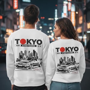 May include: White sweatshirts featuring a car graphic and the word "TOKYO" in black and red. The sweatshirts also display "Street Racing" and Japanese characters. The image shows two people wearing the sweatshirts.