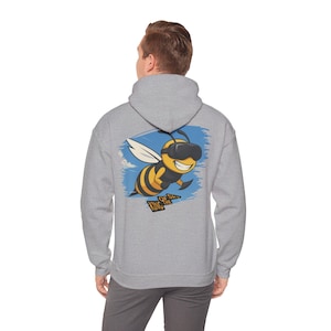 Könnte beinhalten: Ein hellgrauer Kapuzenpullover mit einer Cartoon-Biene, die eine VR-Brille trägt, mit gelben und schwarzen Streifen und dem Text "KING OF SK" auf dem Rücken. Die Biene ist vor einem blauen Himmelshintergrund platziert.