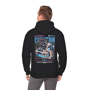 Könnte beinhalten: Schwarzer Kapuzenpullover mit einer Grafik eines Autos und einer Person in Schuluniform. Das Design enthält das Wort "EVOLUTION" in einer stilisierten Schriftart, mit japanischem Text und Sternen.