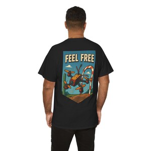 Puede incluir: Camiseta negra con un gráfico colorido de un dron, un bastón de caramelo y las palabras "FEEL FREE" en un rectángulo azul. El dron tiene hélices naranjas y una cámara. El diseño está en la parte posterior de la camiseta.