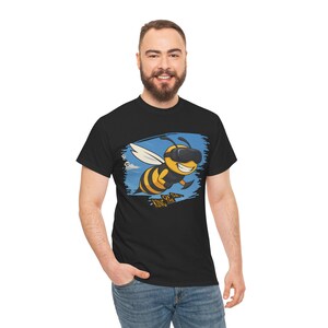 Könnte beinhalten: Schwarzes T-Shirt mit einer Cartoon-Biene, die eine VR-Brille trägt. Die Biene hat gelbe und schwarze Streifen, weiße Flügel und ein lächelndes Gesicht. Das Design umfasst einen blauen Himmelshintergrund und den Text "KING BEE".