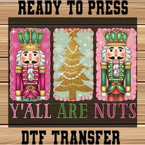 May include: A DTF transfer design featuring a Christmas theme. The design includes two nutcrackers in pink and green uniforms, and a gold Christmas tree. The text "READY TO PRESS" and "Y'ALL ARE NUTS" are displayed above and below the images.