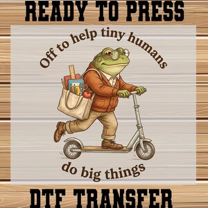 May include: A DTF transfer featuring a cartoon frog riding a scooter, wearing glasses and a sweater, with a tote bag filled with school supplies. Text reads "Ready to Press", "Off to help tiny humans do big things", and "DTF TRANSFER".
