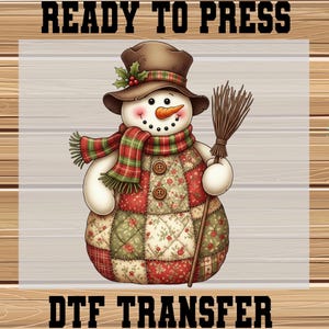 May include: A whimsical snowman design with a brown hat, scarf, and patchwork body. The snowman holds a broom and has a carrot nose. The text "READY TO PRESS" and "DTF TRANSFER" are displayed above and below the snowman.