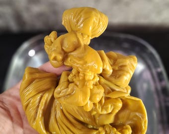 May include: A solid, golden-yellow wax sculpture featuring a complex, organic, and folded texture. The object has a smooth, slightly glossy surface with numerous intricate ridges, curves, and layered sections that create a dense, abstract form.